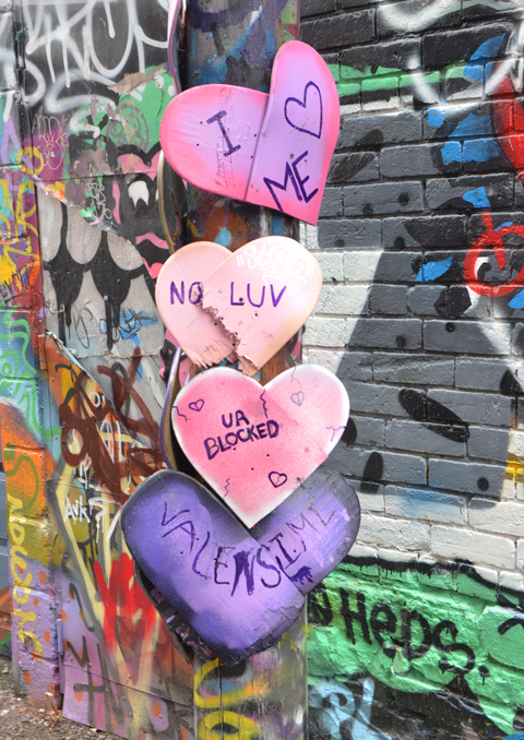on a utility pole in Graffiti alley, there are 4 paper hearts in pink and purple, with words written on them - I love me, no luv, 
