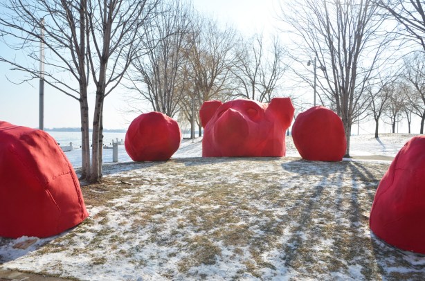a large red head, and four red paws of a bear arranged to look like its on its back and that the bear is partially covered by the snow covered ground. 