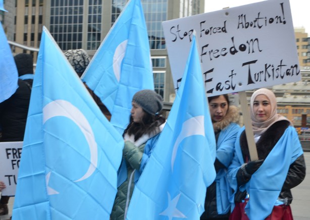 women holding the blue and white flag of East Turkestan, also a sign that says stopped forced abortion in East Turkistan, wearing head scarves