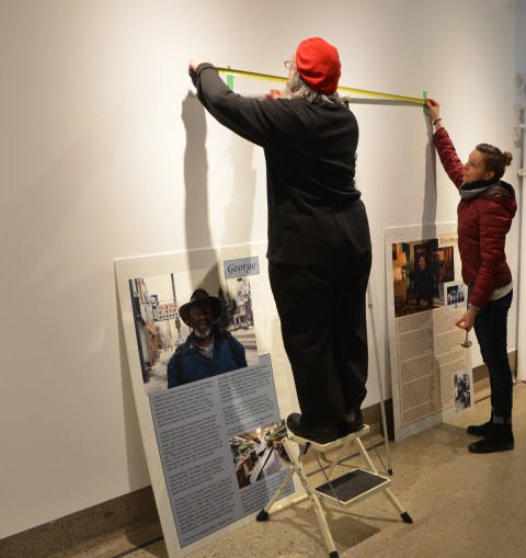 two people hanging pictures in an art gallery 