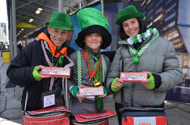 three teenagers selling candy at the parade, all dressed in green hats and other St. Patricks day stuff, 