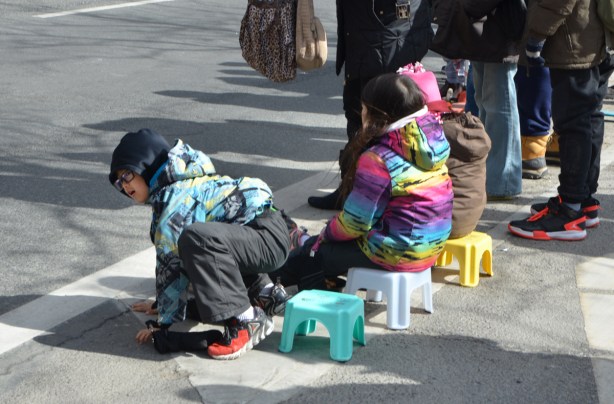three kids sitting on little plastic stools watching a parade, 
