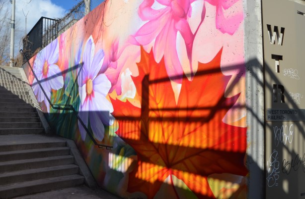 colourful mural outside beside a staircase, large flowers and leaves including an orange maple leaf