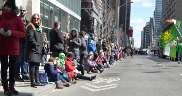 a group of people sitting on the sidewalk as a parade passes by on Bloor Street in Toronto 