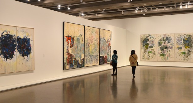 two women looking at large paintings in an art gallery 