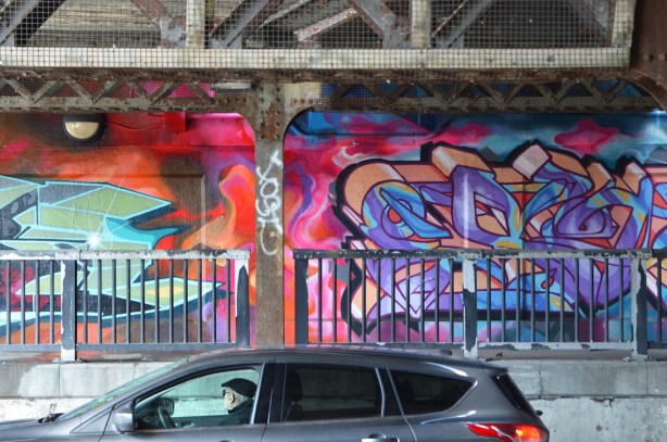 car stopped in traffic under railway bridge, driver is looking at the mural that is painted under the underpass
