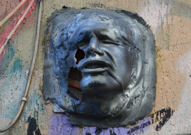 a three D sculpture of a man's face, on a wall, outside, graffiti, forlorn expression on his face 