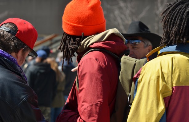 three men with dreadlocks and bright coloured toques, backs to camera, over one shoulder is an older man looking close to the camera