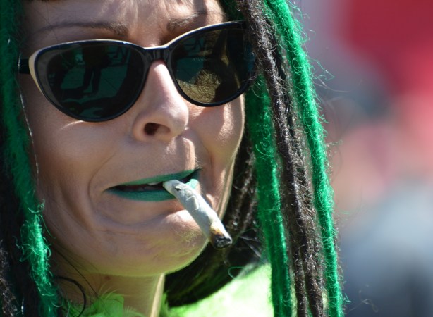 woman with dark sunglasses and black and green dreadlocks smokes a joint, close up photo of her face
