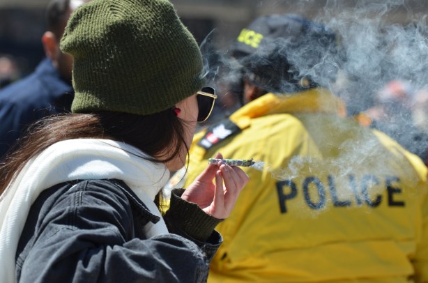 a woman in a green hat smokes a joint behind the back of a policeman in a yellow jacket.