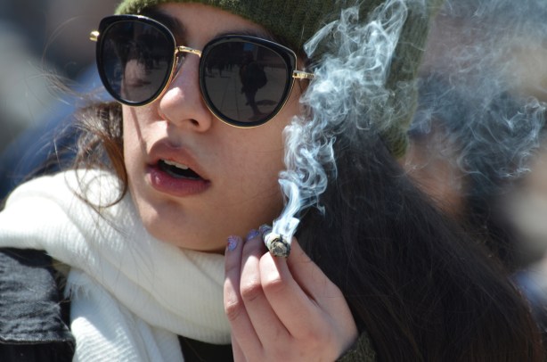 a young woman with sunglasses and a white scarf around her neck smokes a joint,
