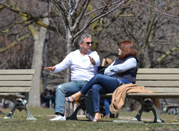 an older couple sitting on a bench in a park, talking to each other, the man is using his arms expressively