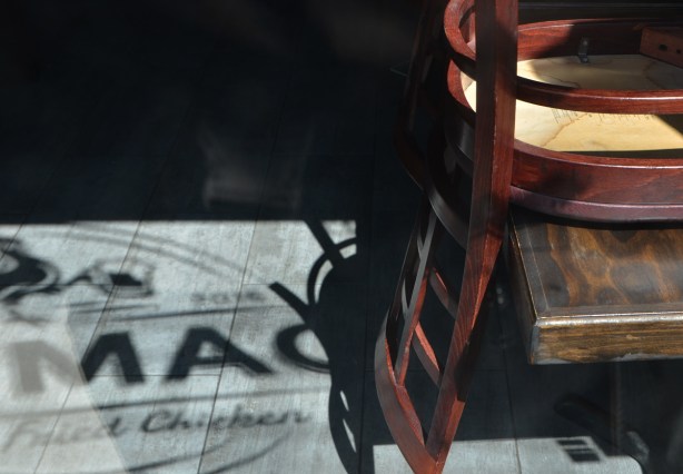 looking into the window of a fried chicken restaurant, chair upside down on table, words on the window show up on the floor because of the sunlight coming in the window