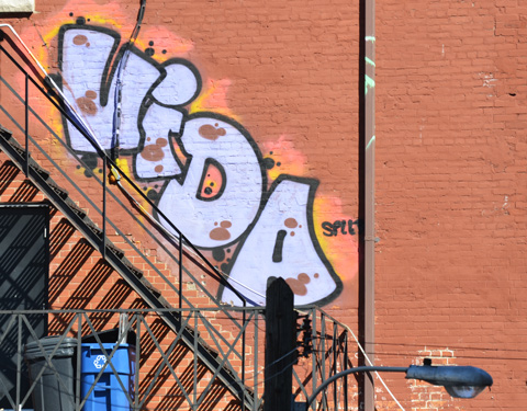street art graffiti that says vida in large letters along the side of a metal staircase, upper story of an orange brick building 