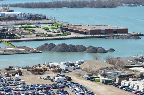 view from higher, over Keating channel, Essroc quay and towards Centre Island, Port lands in Toronto, mounds of gravel in the water, parked cars, boats in the water, light industrical development, trees, 