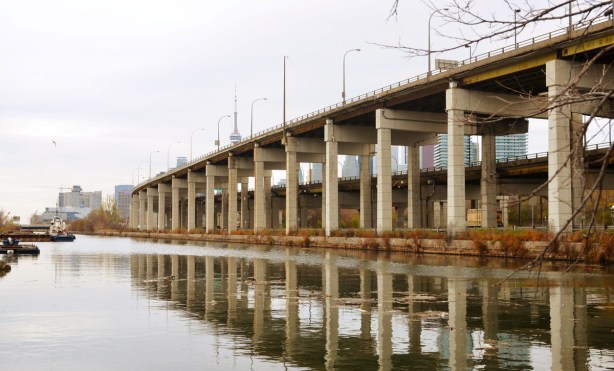 raised expressway road on concrete pillars, runs above another road and beside a channel of water, CH tower and downtown Toronto in the distance