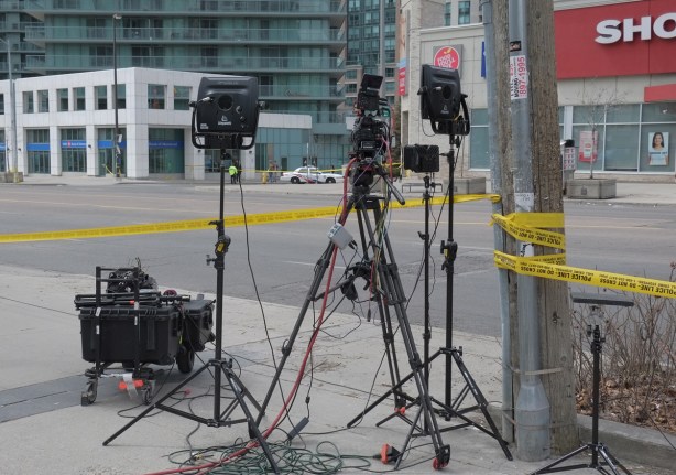camera, and lights on tripods abeside Yonge Street, yellow police tape blocking the street, police car in the background, no traffic