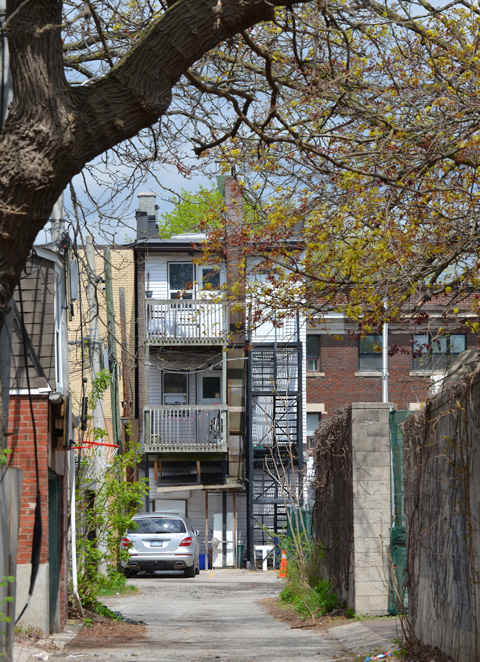 looking down an alley to the back of a triplex (three storeys high) with fire escape stairs and balconies with railings 