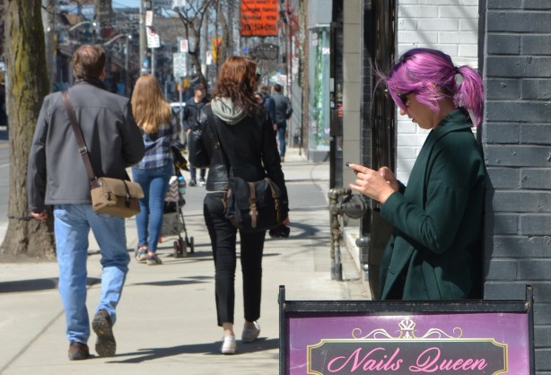 a woman with magenta hair is standing on the sidewalk, back against a wall. 
