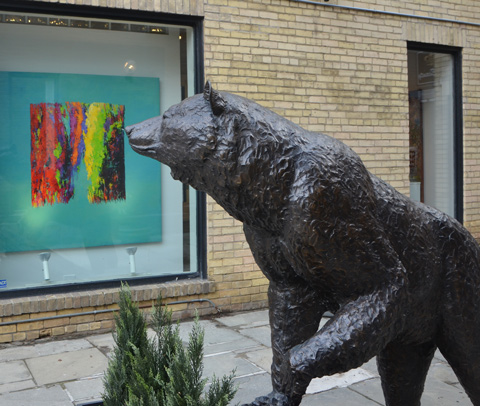 statue of a bear outside, life size, a painting in a glass enclosed box is behind him 