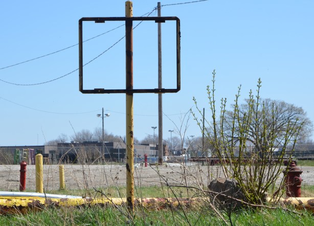 empty rectangular metal frame where a sign once was, on an old yellow rusty pole, vacant land in the background 