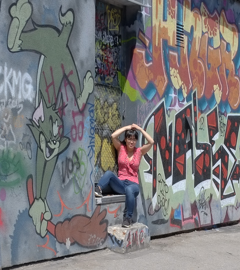a woman in jeans and pink top poses in the doorway of one of the back doors in Graffiti Alley 