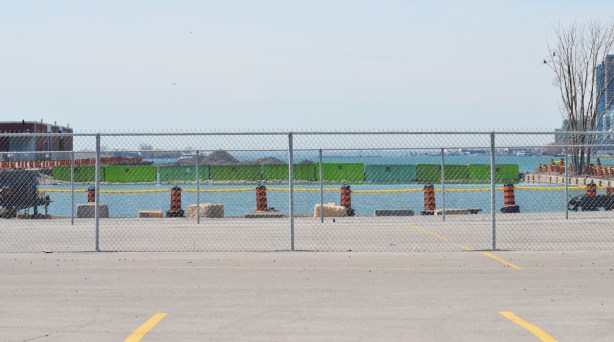 behind a chain link fence, a line of green dumpster bins, laid end to end, stretch across a channel in Lake Ontario, 