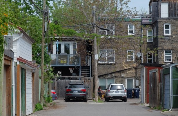 alley view, rear of old three storey brick buildings, apartments on top, stores below, cars parked, 