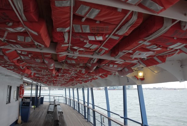 ferry, ceiling is full of orange life jackets, railings along edge, Lake Ontario, benches to sit on but no people 