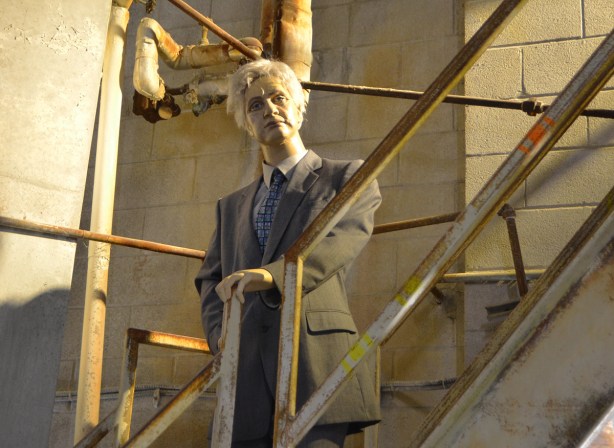 mannequin automatons as part of an art installation in the old Unilever soap factory, concrete floor and walls - an older man standing on the stairs and looking down 