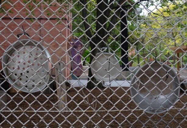 old metal pans attached to a chainlink fence at a school 