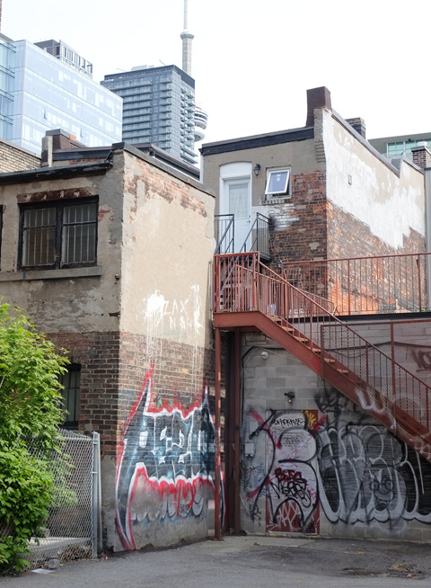 back of old brick buildings, some graffiti, orange metal stair case, CN TOwer in the background 