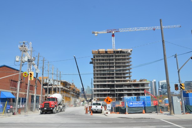cement truck on street in front of construction site, cranes, fences, building about 20 storeys high 