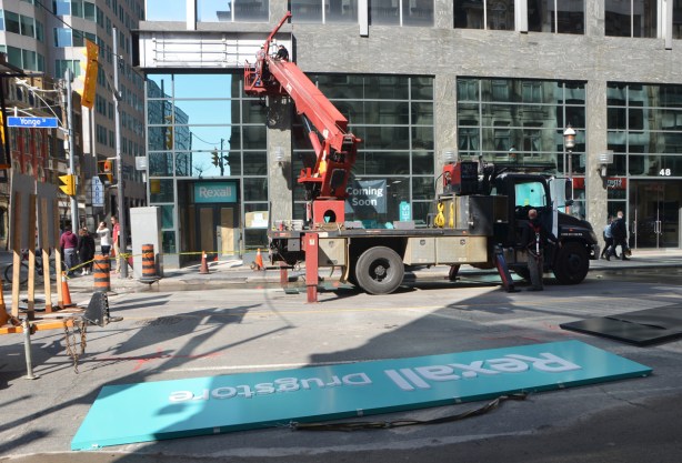 workmen on a lifter install a new sign on the outside of a Rexall drug store. 