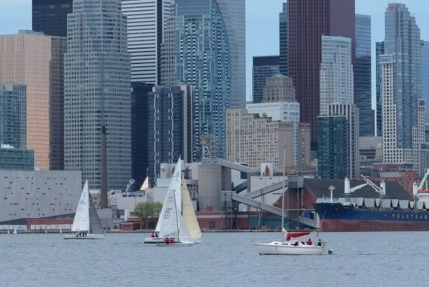 sail boats in Inner Harbour of Lake Ontario, in front of the Toronto skyline with highrises and skyscrapers also ship moored at Redpath Sugar refinery 