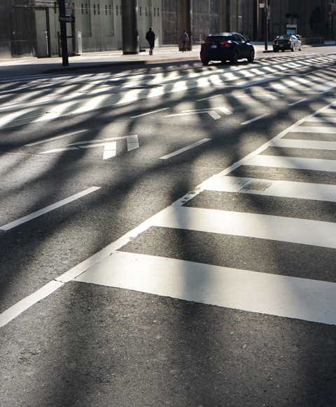 light and shadow patterns produce by low morning sun shining on downtown glass skyscrapers, on the street below with its white lines adding to the pattern