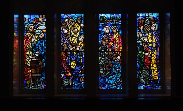 set of four stained glass windows in deep hues of red and blue with some yellow and green, by Gerald Tooke, at St Simons church 