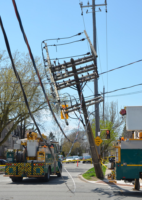 a large pole with a myriad of wires (hydro wires) has started to fall over. wires draping low across the street. hydro trucks on the scene