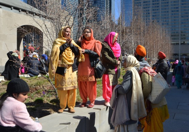 sikh women in pink, orange, and yellow saris, standing outside and socializing 