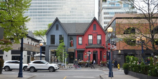 looking down Hazelton Ave towards Yorkville Ave., two older houses, now used as commercial businesses, one half painted blue and the other half is red. 