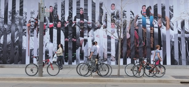 caroline Monnet's large mural on the side of TIFF building, King street, people walking past, bikes parked in front of the art. 