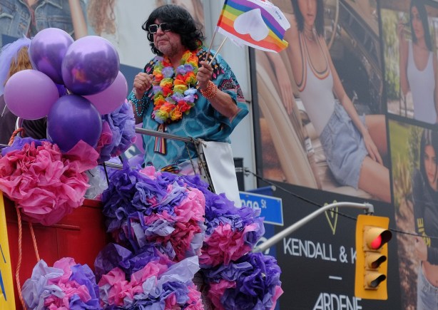 man with flag riding on float in pride parade, lots of pink and purple balloons and ruffles 
