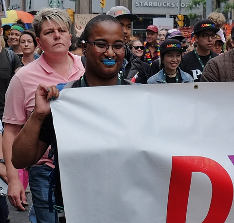 dyke march 2018 - dark brown person wearing blue lipstick holds a white banner 