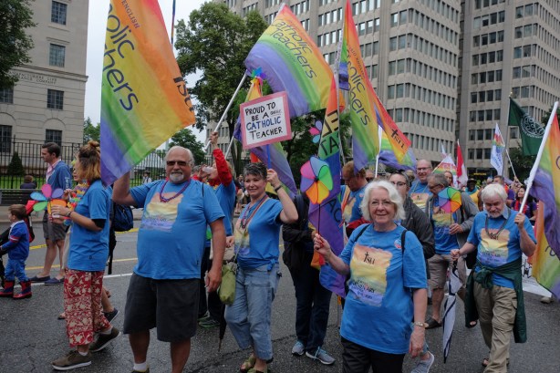 group of people in blue T-shirts and carrying rainbow flags that say proud to be a Catholic teacher 