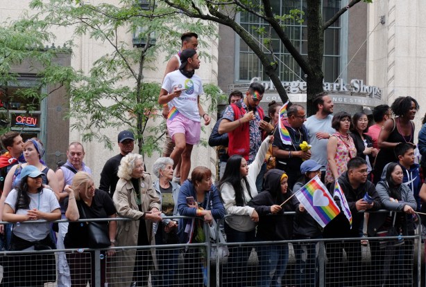 crowds watching the pride parade, all ages, some standing on planters in the middle of Yonge Street, College Park building behind them 