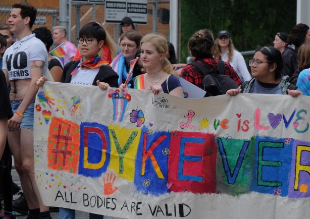 dyke march 2018, banner that says dykeversity, lots of hand prints and hearts decorating it, women carrying it, 