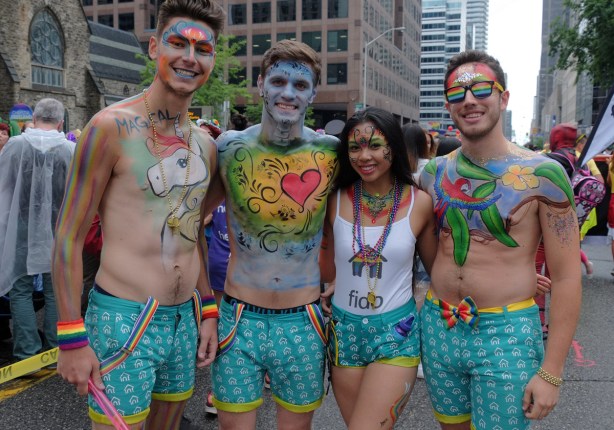 a group of four young people from the fido section of the pride parade, in teal shorts, covered with colourful body paint hearts and stars and rainbows 