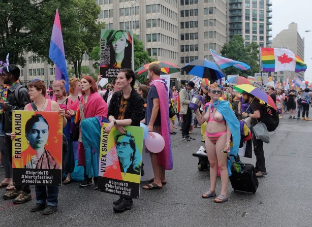 getting ready for the pride parade, a topless woman stands near a group carrying posters, one with Frida Kahlo on it and the other with Vivek Shraya
