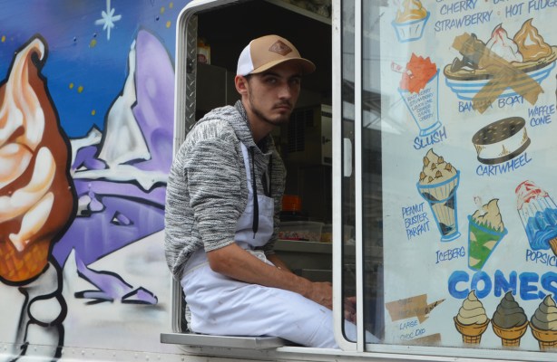 a young man sits in the window of an ice cream truck as he watches the crowd 