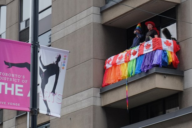 two men stand on a balcony of the Courtyard by Marriott Hotel on Yonge street, decorated balcony with Canadian flags and rainbow coloured paper or fabric. 